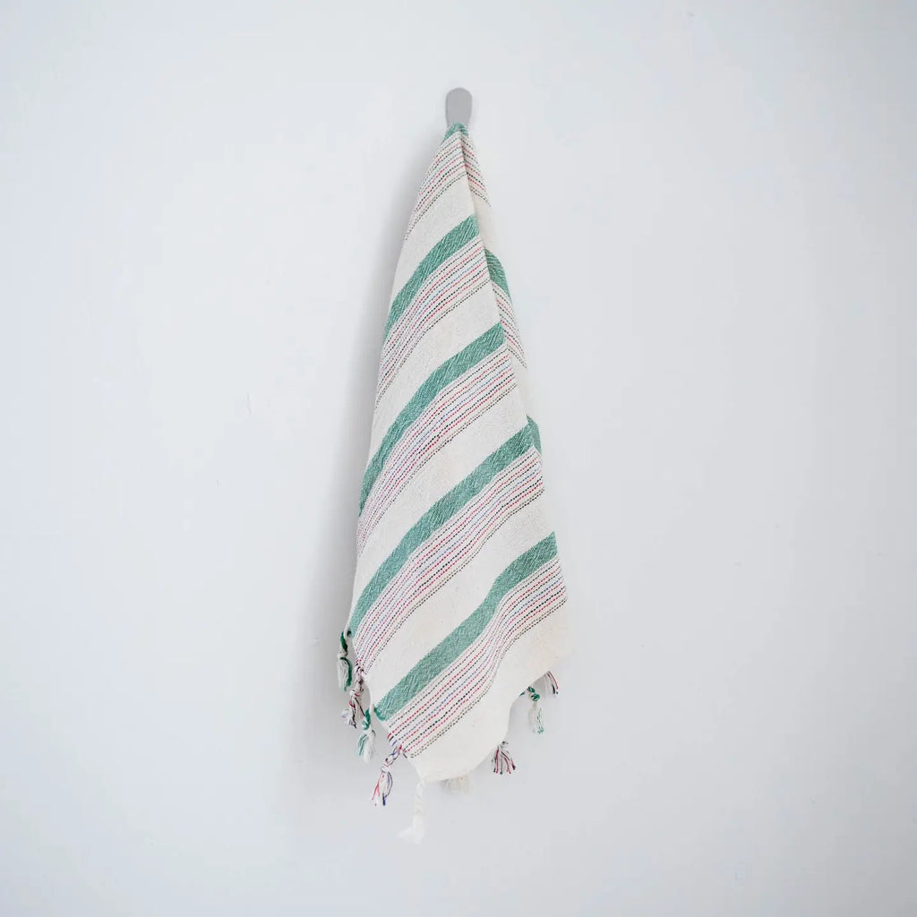 Striped towel with tassels hanging on a hook against a white background