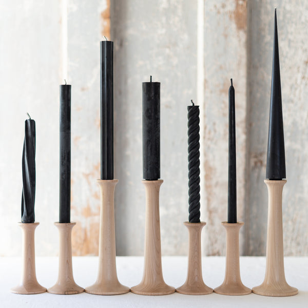A selection of black taper candles arranged by design, with natural and twisted patterns, made from beeswax, displayed on candle holders.