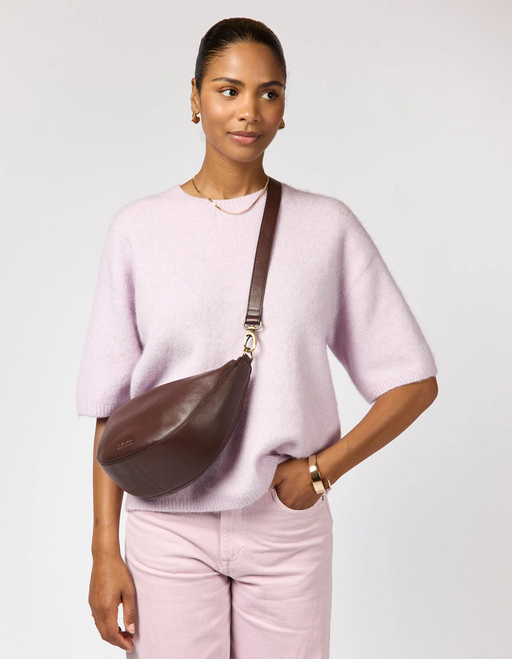 Woman wearing a pink sweater and pants with a brown leather bag on a light gray background