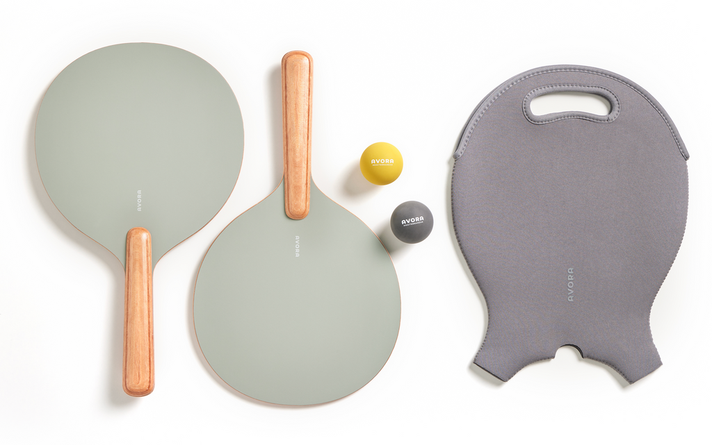 Two green paddle ball paddles with beige handles, two yellow and gray balls, and a gray carrying case for a beach bat set.