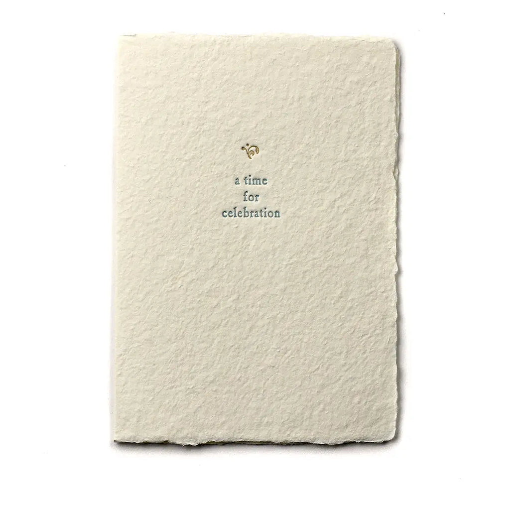 A beige handmade paper card with golden ornament and blue text, showing a folded card with a cream envelope, placed on a white background.