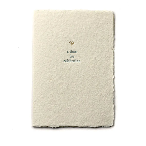 A beige handmade paper card with golden ornament and blue text, showing a folded card with a cream envelope, placed on a white background.