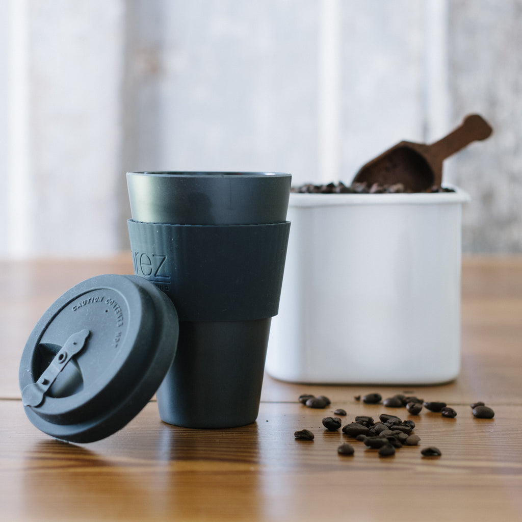 enamel storage container with acacia wood lid filled with coffee beans next to a travel mug