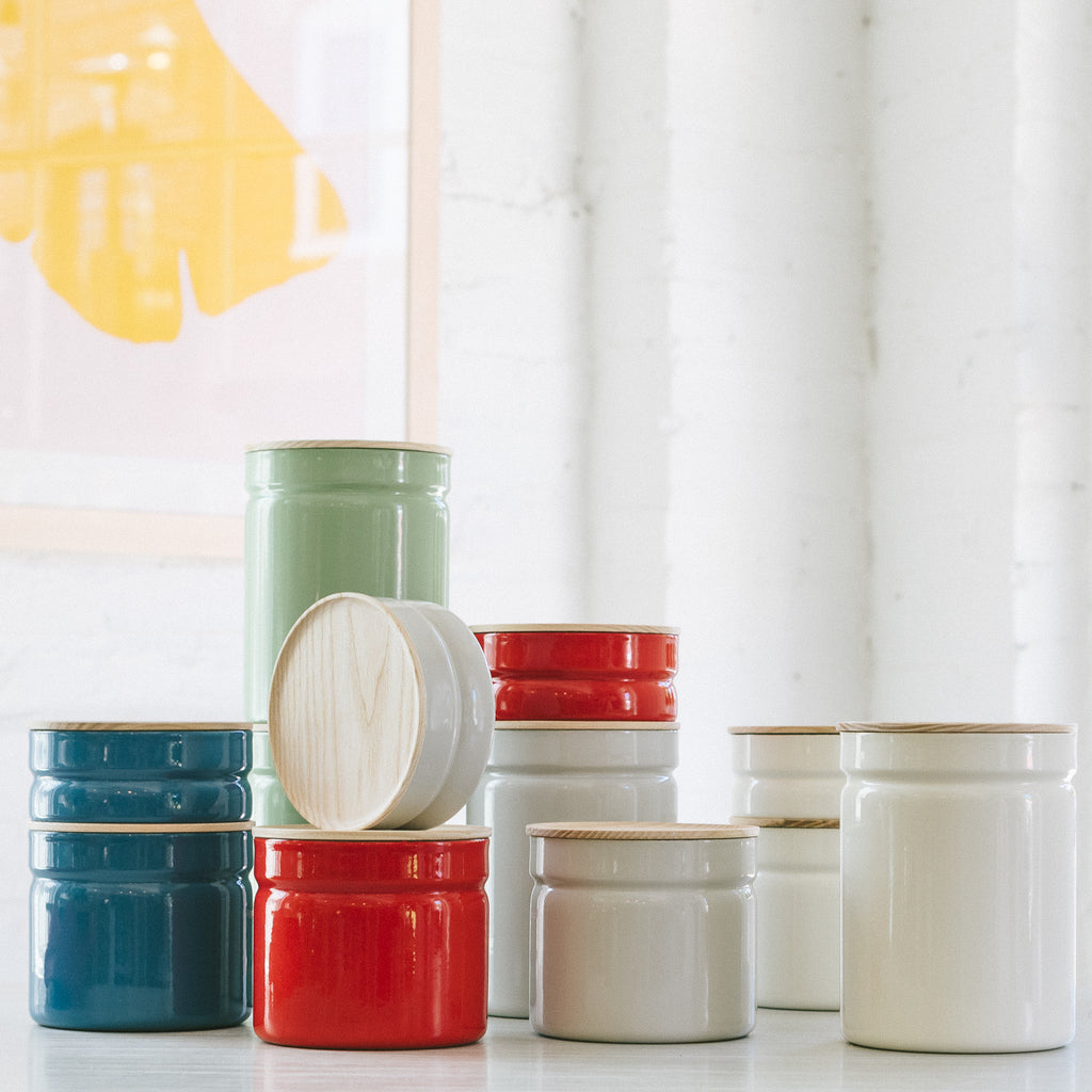 A collection of enameled porcelain food storage containers in various colors including blue, red, green, and white, with their respective lids on or off.