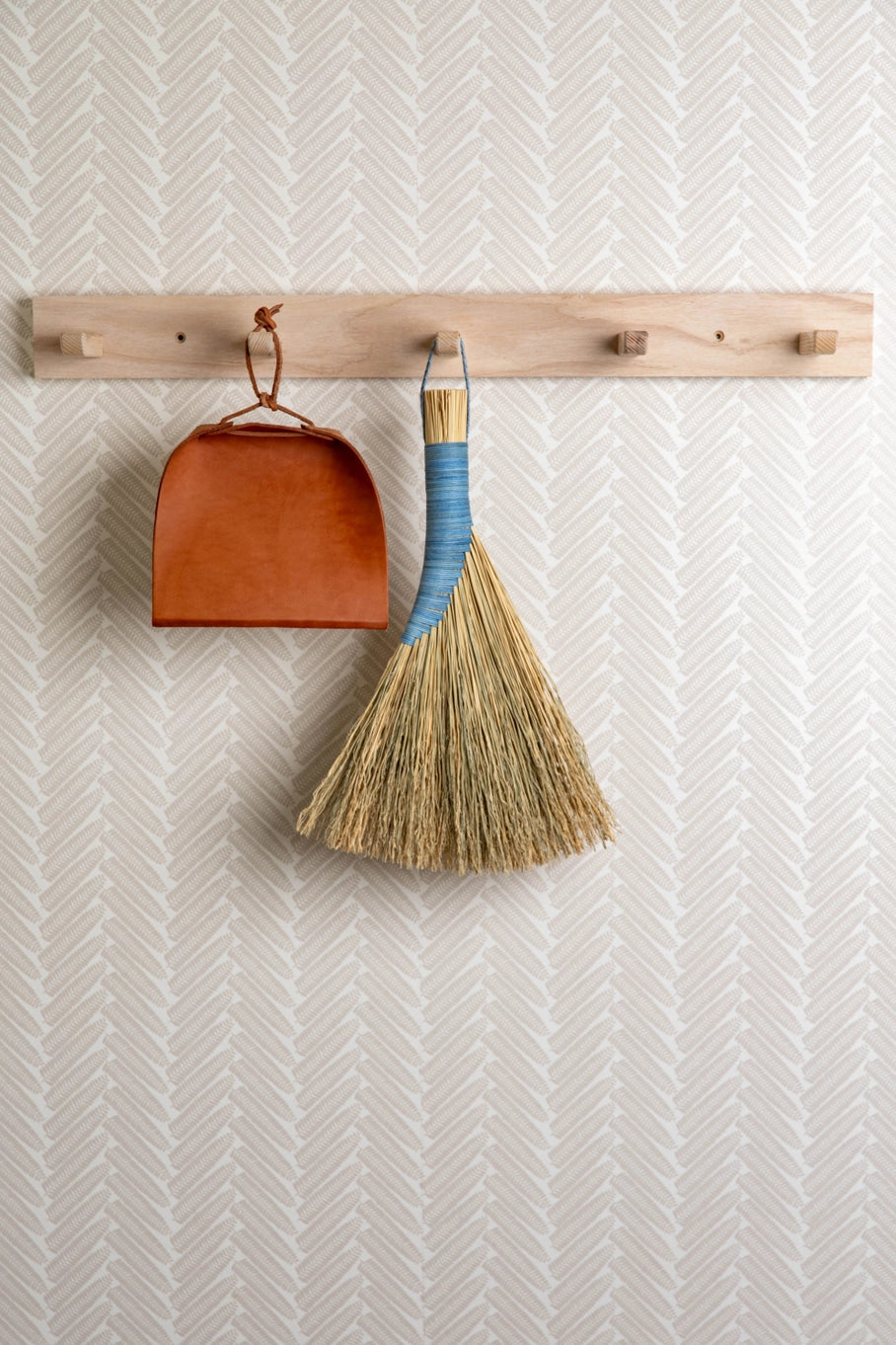 Broom and dustpan hanging on a wooden rack against a textured wall.