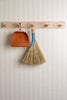 Broom and dustpan hanging on a wooden rack against a textured wall.