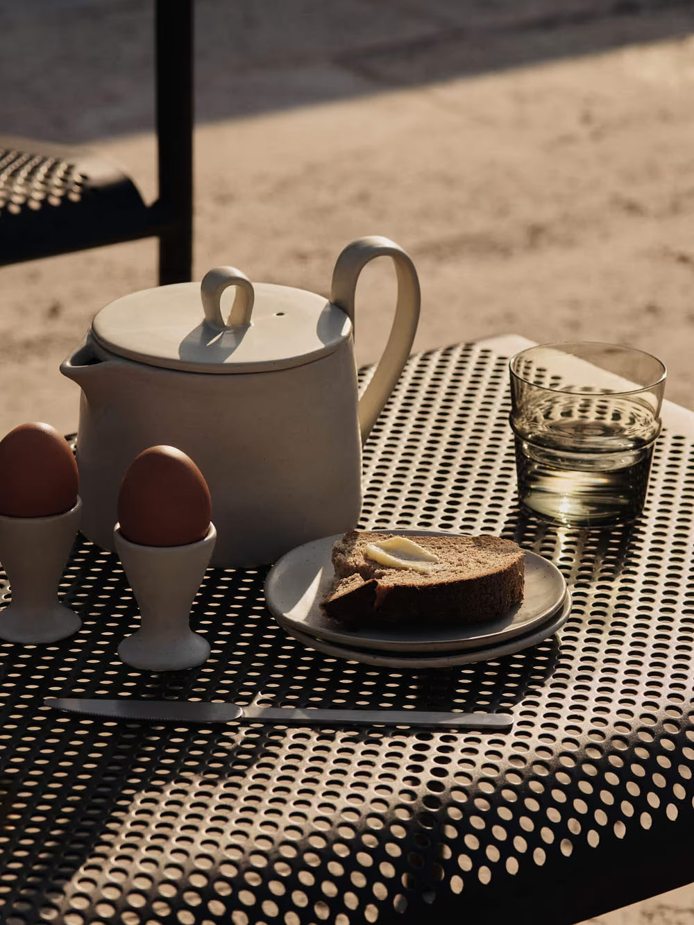 Teapot, eggs, toast, and glass on a metal table outdoors.