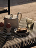 Teapot, eggs, toast, and glass on a metal table outdoors.