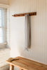 Wooden coat rack with a checkered towel hanging on a wall next to a wooden bench.