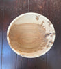 A round handcrafted wooden bowl with natural wood grain patterns, photographed from directly above on a dark wooden plank surface.