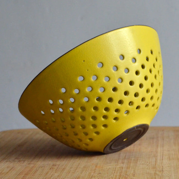 Yellow colander on a wooden surface with a gray background