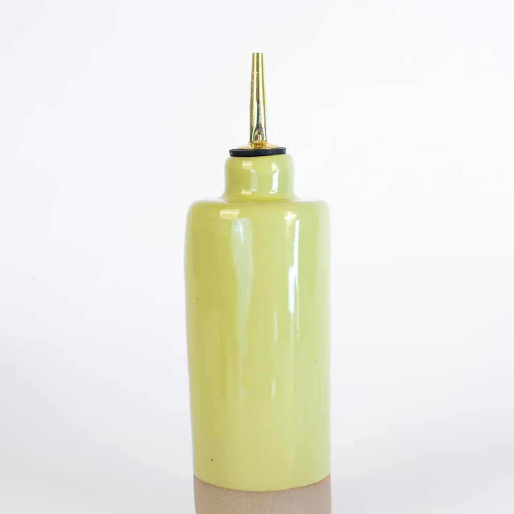 Yellow ceramic condiment bottle with a gold nozzle on a white background