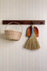 Wicker basket, broom, and dustpan hanging on a wooden rack against a white wall with a subtle pattern.