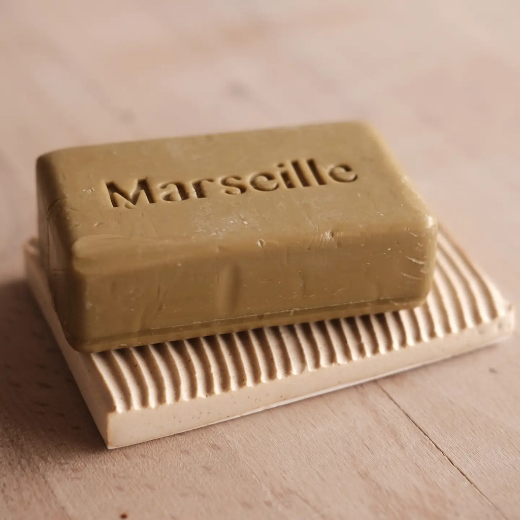 Bar of Marseille soap on a ceramic soap dish with 'Marseille' branding.