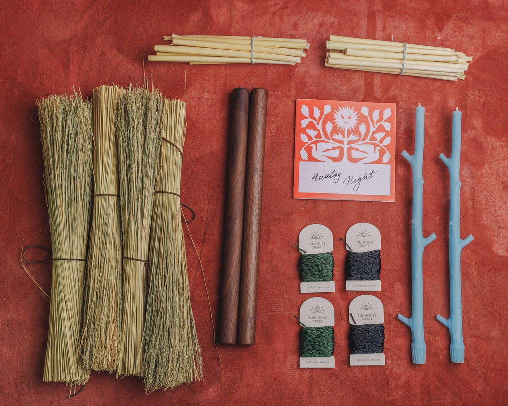 A flat-lay arrangement of craft or decorative materials on a textured red-orange background: four small straw bundles, two dark wooden sticks, a folded card reading 'endless night,' two pale blue branch-shaped pieces, and four spools of thread in green, navy, gray, and white. No person, animal, or real environment is present, so this is Product/Packaging rather than Lifestyle.