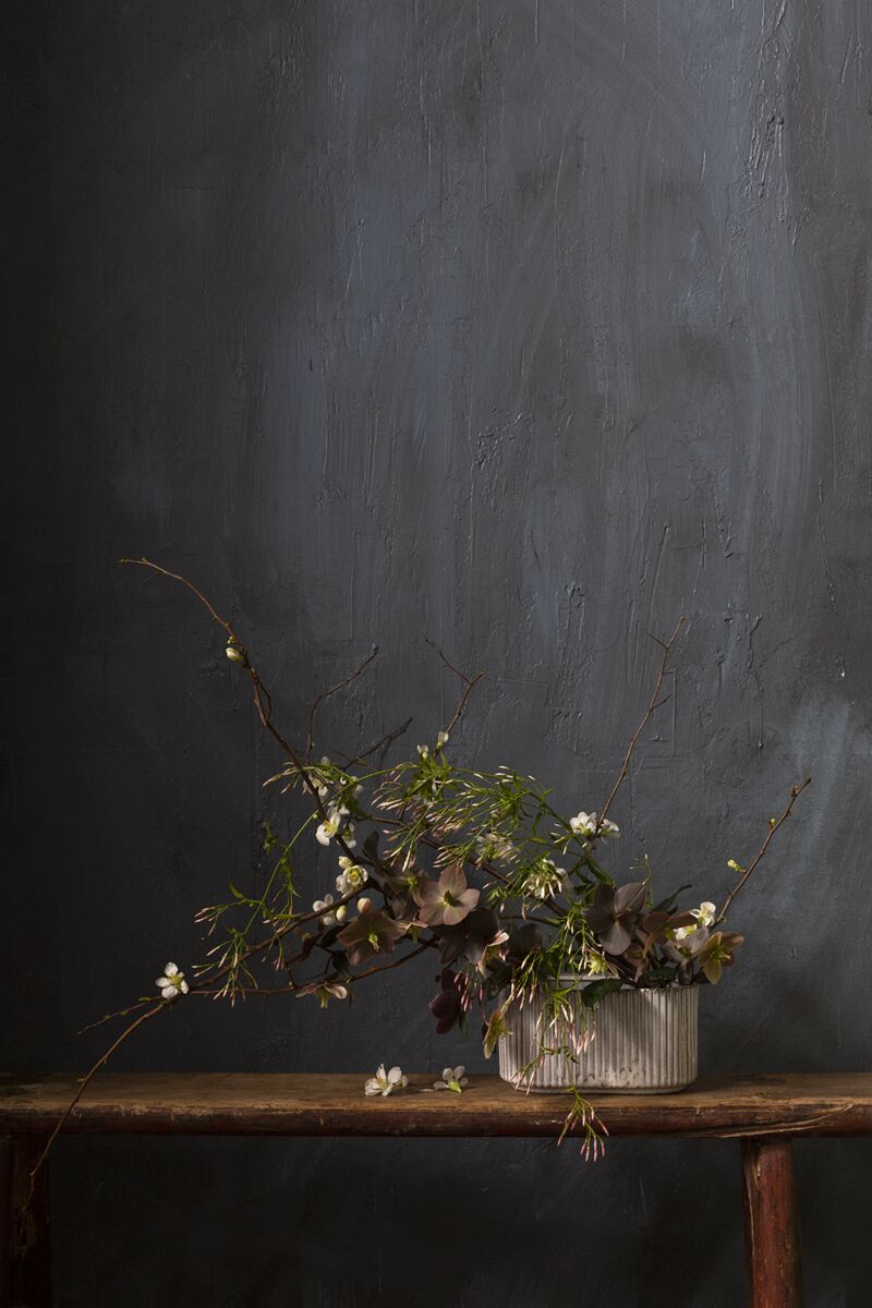 Dried floral arrangement in a ceramic vase on a wooden table against a dark gray wall.