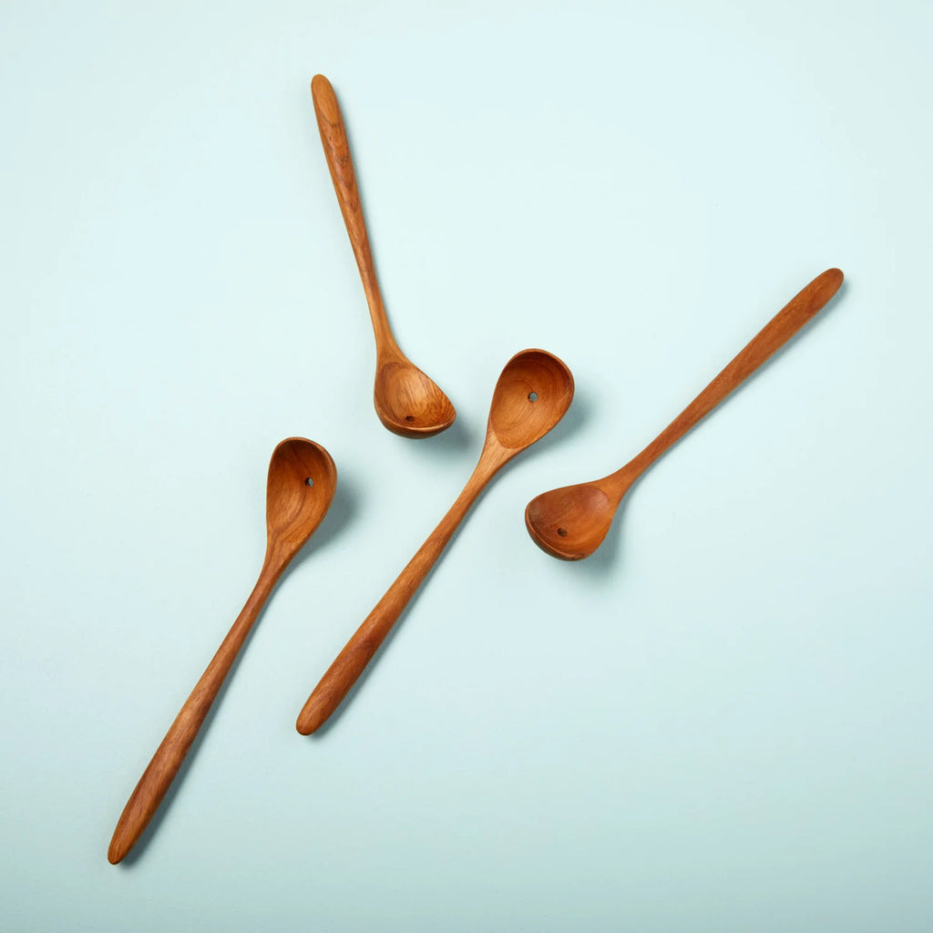 four spoons made from teak wood with a whole in the bottom of each spoon to drain liquids. The spoons sits on a blue background