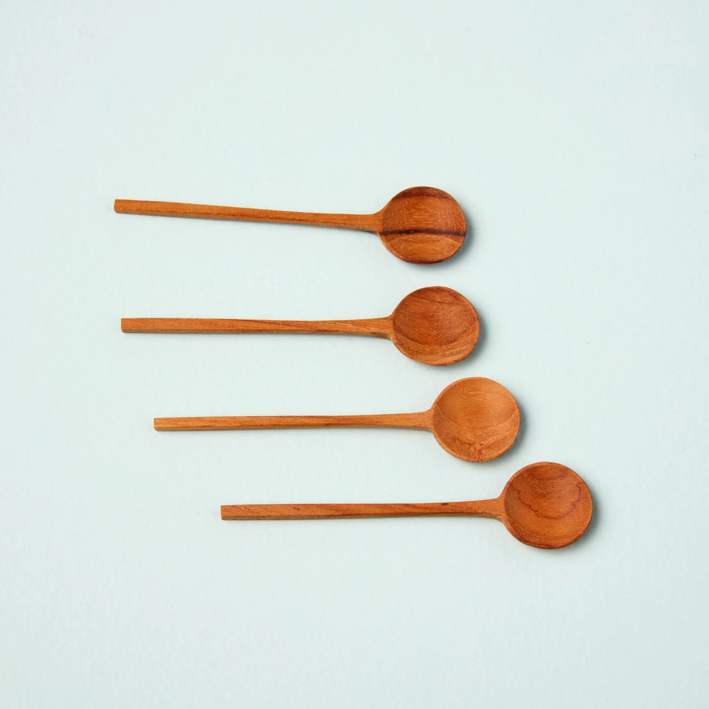 Four thin spoons made from teak wood laying on a flat blue surface