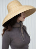 Person wearing a wide-brimmed straw hat and gray top with a scarf against a white background