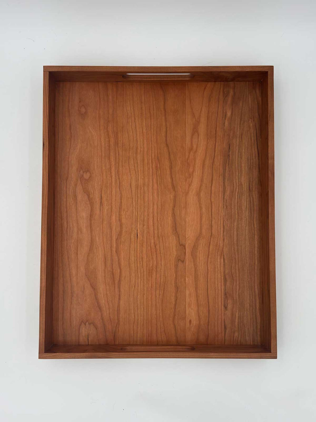 A rectangular wooden serving tray with a warm medium-brown wood grain finish and a small recessed handle cutout at the top edge, shown against a plain white background.