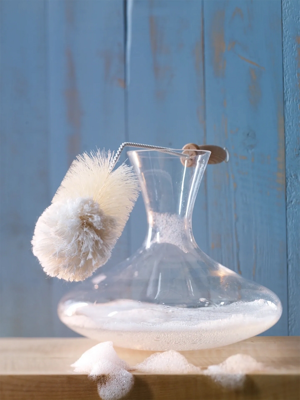 Clear glass carafe with a brush on a wooden surface against a blue wooden background