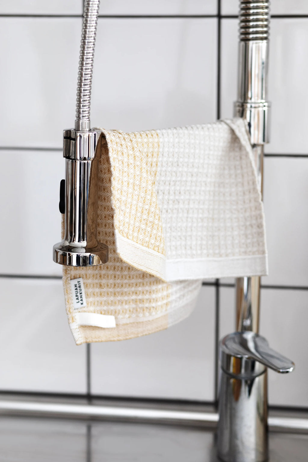 Yellow-linen kitchen towel hanging on a silver kitchen faucet. 
