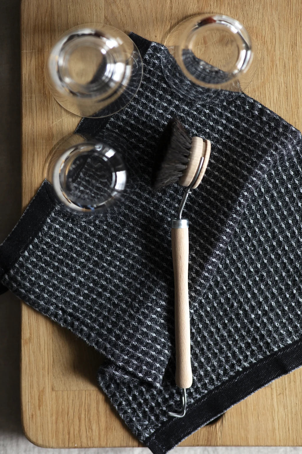 kitchen towel on a wooden cutting board with glasses and a dish brush. 
