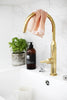 Dish towel hanging on copper faucet in a bright kitchen. Basil plant and soap in the background. 