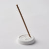 White incense holder with a single incense stick on a light gray background