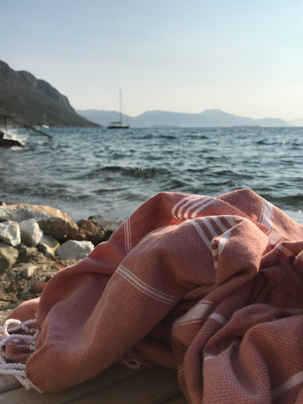Pink towel with white stripes on a wooden surface by the sea