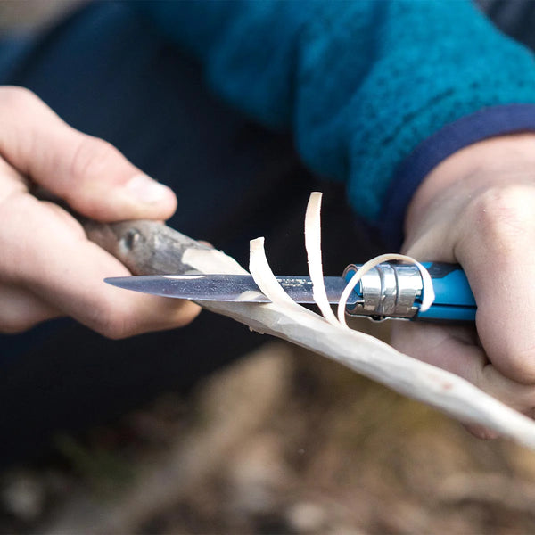 Person using a kids knife to cut stick with a blurred background
