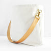 A white canvas tote bag with a wide, tan leather shoulder strap and gold-tone metal hardware, shown on a clean white background.