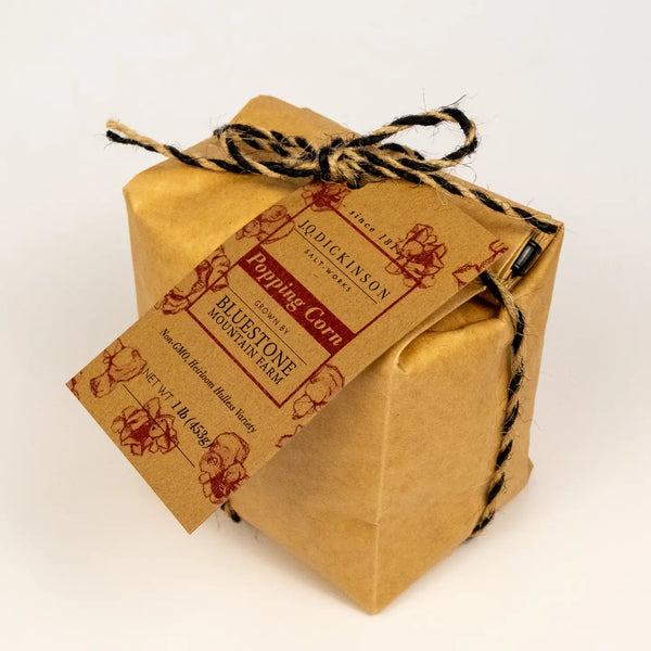 A square kraft paper gift box wrapped with black-and-brown twine and a printed paper tag reading 'Popping Corn Bluestone Mountain Farm,' photographed on a clean white background.