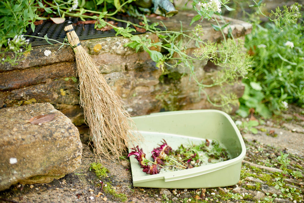 Garden scene with a broom and compost bin filled with garden waste.