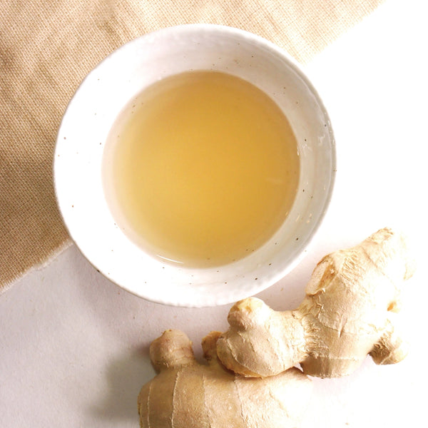 Ginger tea in a white bowl with fresh ginger root on a light background