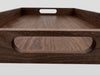 Close-up of a dark brown wooden serving tray with a natural wood grain finish and a cutout handle, shown against a light gray background.