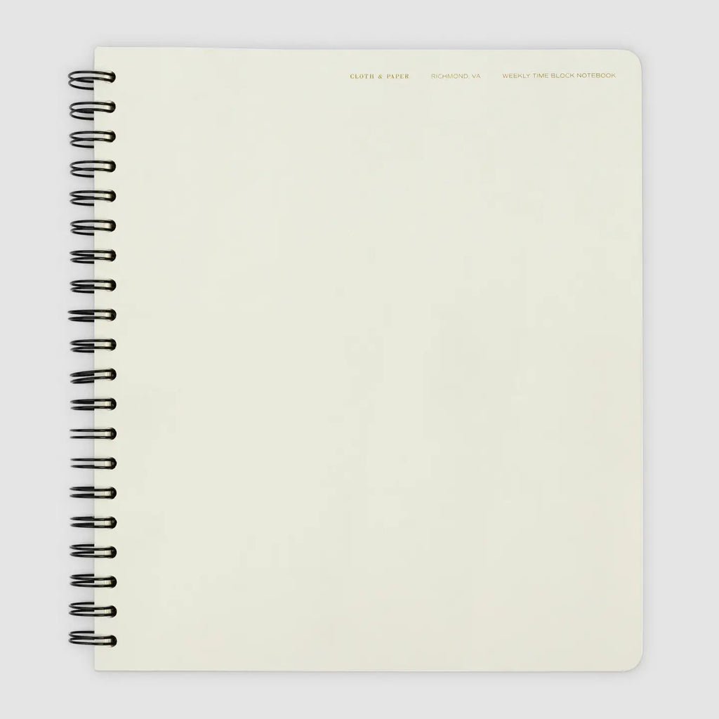 A cream-colored spiral-bound notebook with a black wire coil binding, shown from a top-down view on a light gray background.
