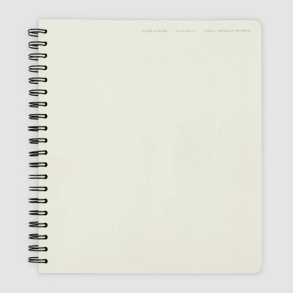 A cream-colored spiral-bound notebook with a black wire coil binding, shown from a top-down view on a light gray background.