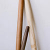Three wooden rolling pins in natural light brown, cream, and dark brown tones, arranged vertically against a plain off-white background.