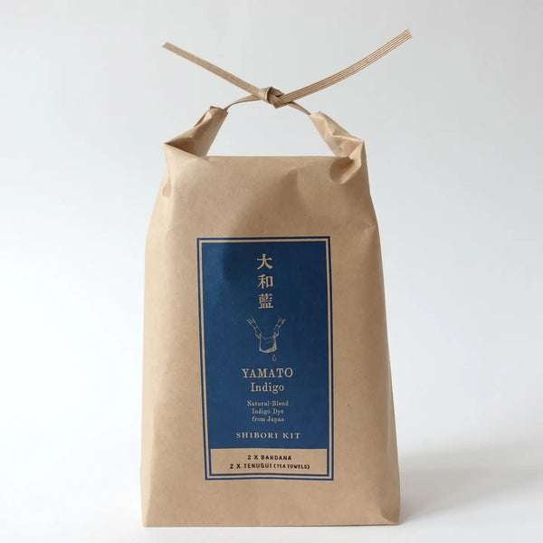 A kraft paper bag package tied with a thin ribbon at the top, featuring a blue front label with Japanese text and the English brand/product name Yamato Indigo.