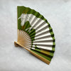 Handheld fan with green and brown and white cow design featuring a goat on a light gray background