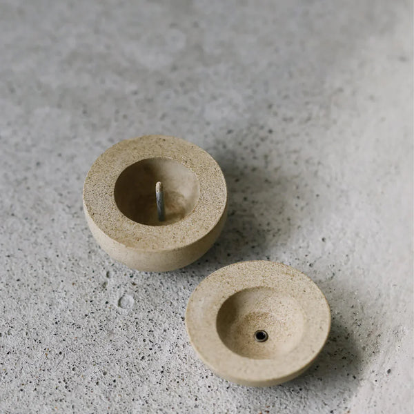 Two beige stone candle holders on a textured gray surface