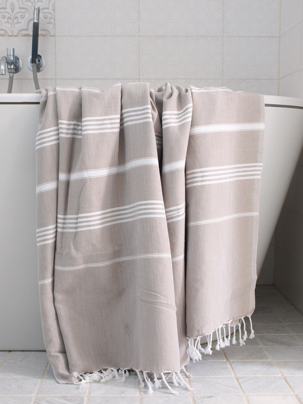 Beige towel with white stripes draped over a bathtub in a bathroom setting.