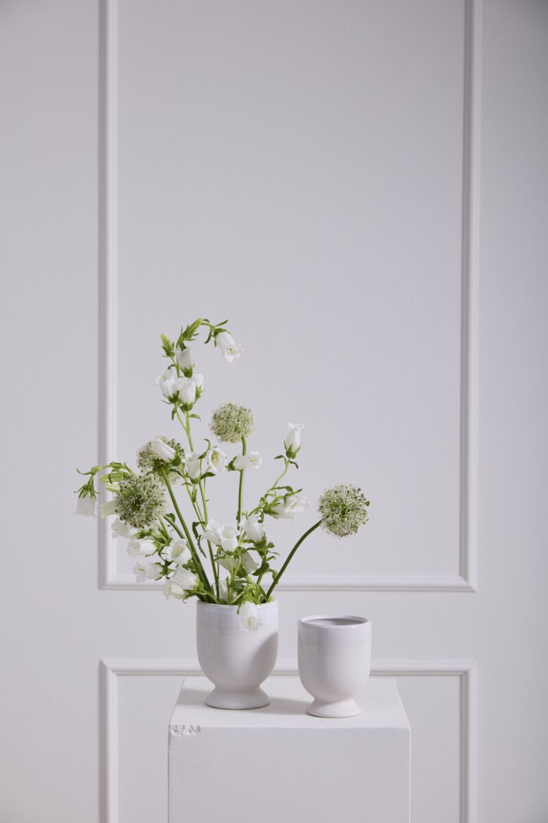 Two white egg-shaped vases with greenery on a light gray paneled wall.