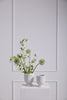 Two white egg-shaped vases with greenery on a light gray paneled wall.