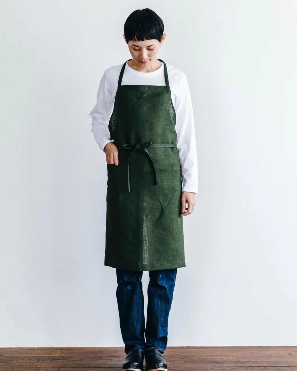 Person wearing a green apron over a white shirt and dark pants on a plain background