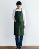 Person wearing a green apron over a white shirt and dark pants on a plain background