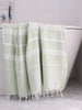 light green towel with white stripes and tassels hanging on a bath tub in a bathroom.