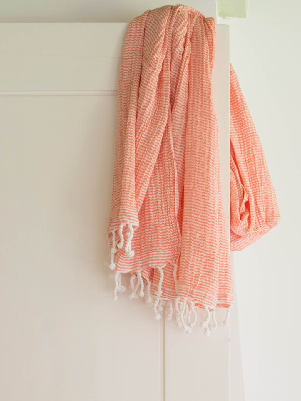 Coral-colored towel with white tassels draped over a white surface