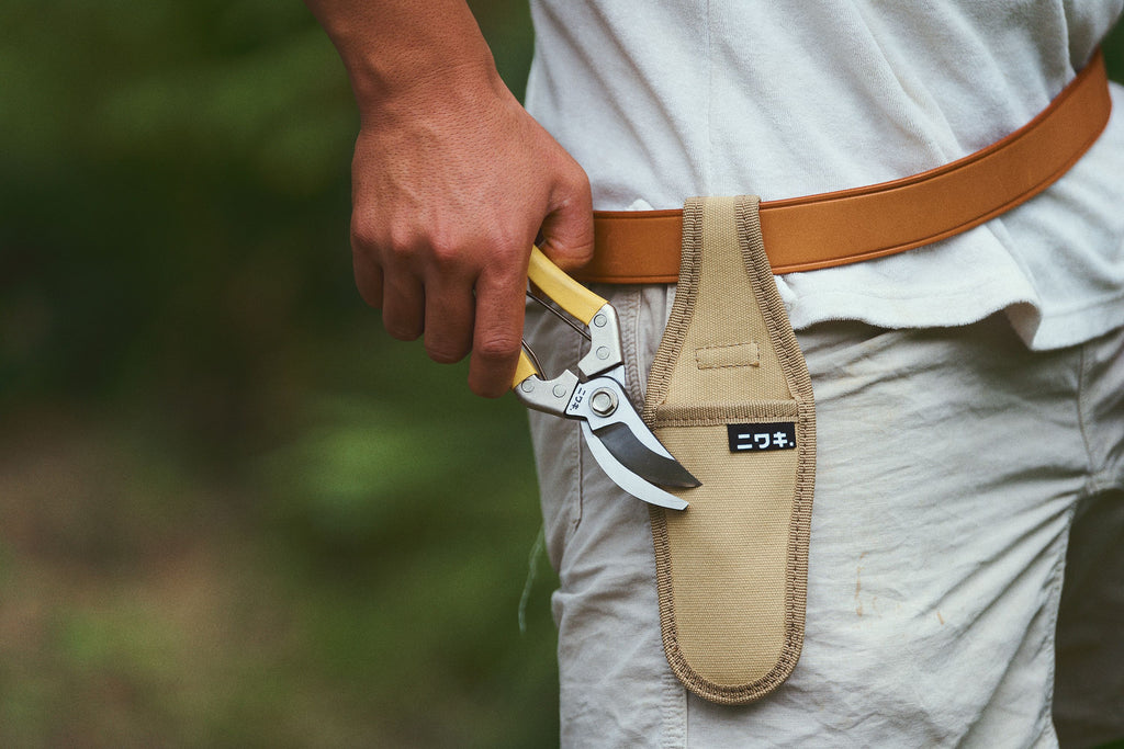 Person holding a pair of pruning shears in a leather sheath with a blurred natural background